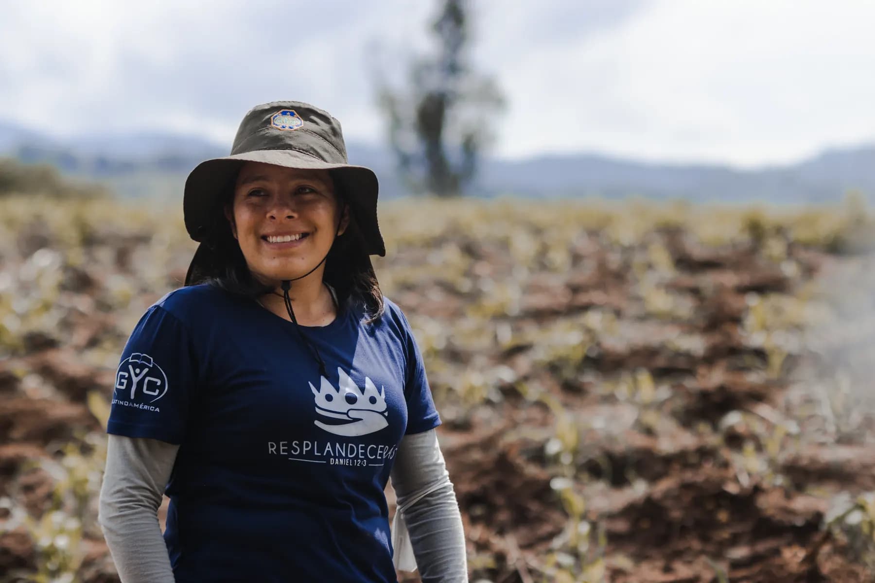 Una joven con camiseta de GYC Guatemala sonriendo durante una jornada de misión en el campo